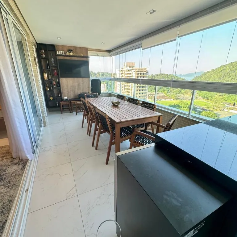 Varanda gourmet com churrasqueira, vista mar e panorâmica para o morro de Xixová, envidraçada e cortina blackout.